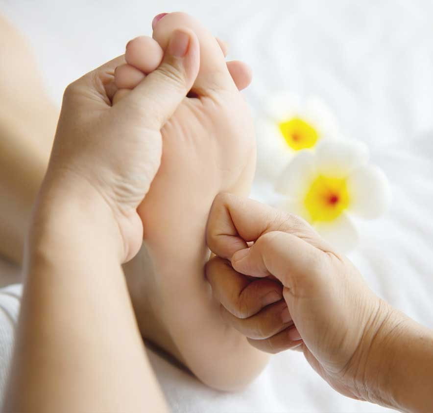 Practitioner pressing points on the sole of a foot, with frangipani flowers in the background